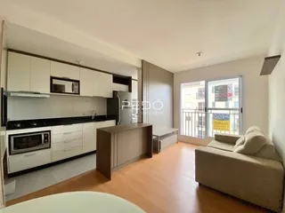 Sala de estar e cozinha com piso de madeira e armários brancos.