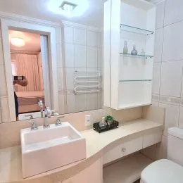 Foto de um banheiro com bancada branca e revestimento de azulejos brancos.