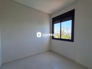 Ambiente interno com paredes brancas e uma grande janela com vista para a vegetação.