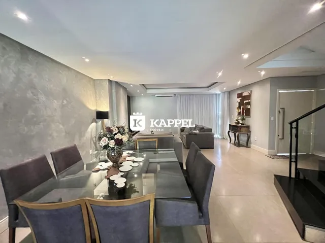Sala de jantar ampla com mesa de vidro e cadeiras escuras em um ambiente moderno.