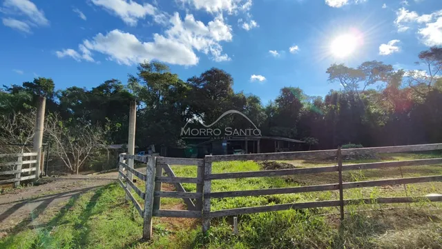 Vista externa da propriedade com cerca de madeira e vegetação ao fundo.