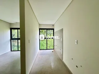Corredor interno com paredes brancas e piso claro, com uma porta de vidro que dá acesso a uma área externa com vegetação.