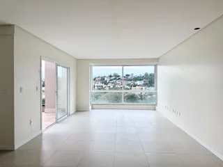 Uma sala ampla com piso de porcelanato e grande janela com vista para a paisagem urbana.