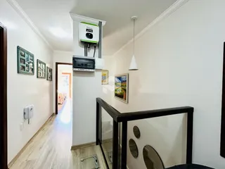 Corredor interno de uma residência com piso de madeira clara e paredes brancas.
