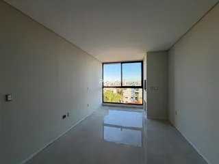 Ambiente interno com paredes brancas e grande janela de vista para a cidade.