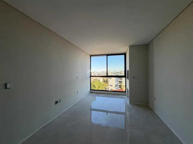 Ambiente interno com paredes brancas e grande janela de vista para a cidade.