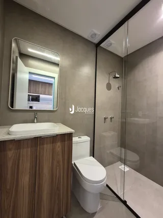 Banheiro com bancada de madeira e box de vidro transparente.