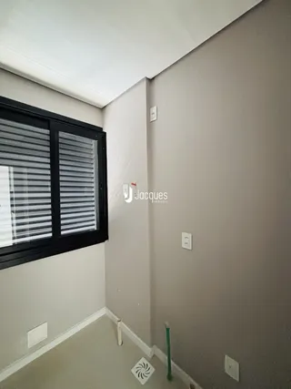 Vista de um canto interno de uma sala com parede clara e janela.