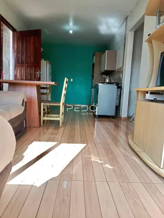 Sala de estar com piso de madeira e cozinha visível ao fundo.