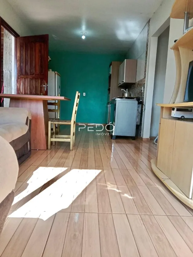 Sala de estar com piso de madeira e cozinha visível ao fundo.