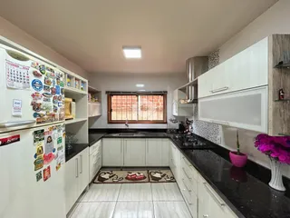 Vista interna de uma cozinha com armários brancos e bancadas escuras.