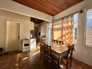 Sala de jantar com mesa de madeira e janelas no interior de uma residência.