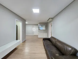 Vista de um corredor interno com piso de madeira clara e um sofá.
