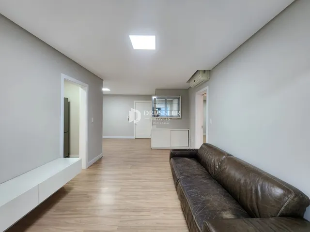 Vista de um corredor interno com piso de madeira clara e um sofá.