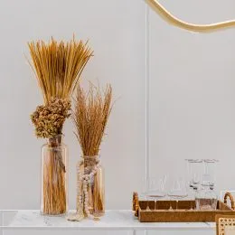 Ramos secos decorativos em um vaso sobre uma parede clara.