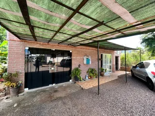 Vista da fachada de uma residência com estrutura de pergolado e piso de cascalho.