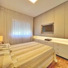 Quarto com cama e cortinas claras em um ambiente bem iluminado.