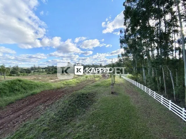 Vista externa de um terreno com grama e cerca branca ao lado de uma área arborizada.