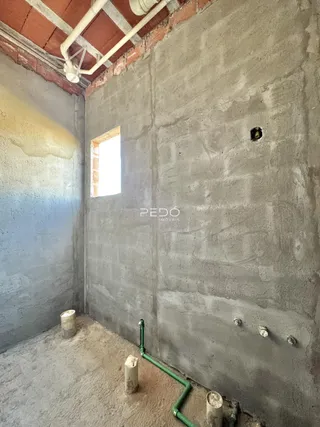 Interior de uma sala com paredes de concreto aparente e piso cru.