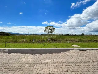 Vista externa mostrando um campo gramado e paisagem distante sob um céu azul.