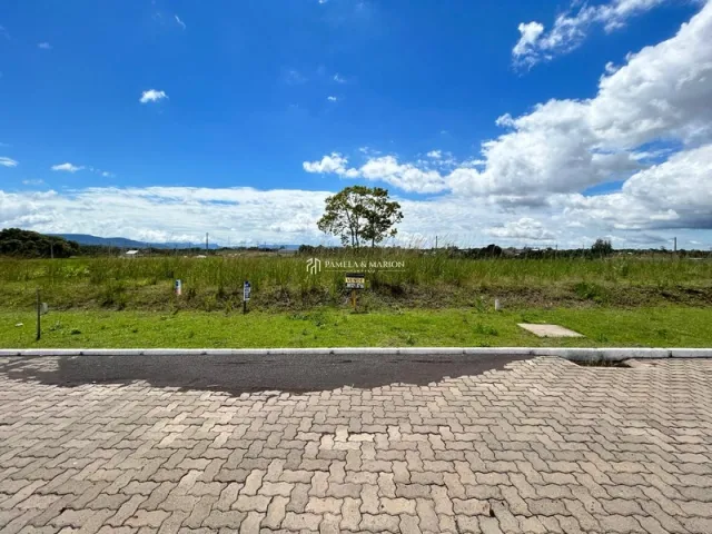 Vista externa mostrando um campo gramado e paisagem distante sob um céu azul.