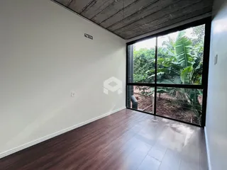 Ambiente interno com piso de madeira e grande janela de vista para a vegetação.
