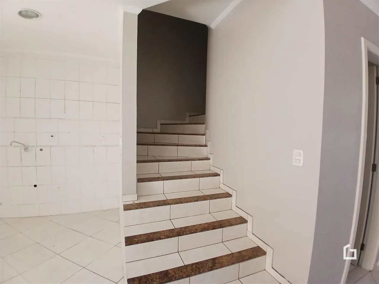Vista de um corredor com escadaria e revestimento de azulejos brancos.