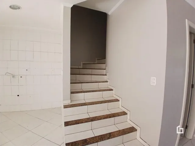 Vista de um corredor com escadaria e revestimento de azulejos brancos.