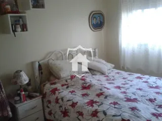 Quarto com cama e janela iluminada por cortinas brancas.