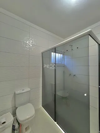 Interior de um banheiro com revestimento cerâmico e box de vidro.