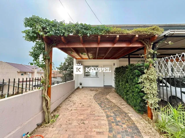 A foto mostra a entrada de uma residência com um pátio coberto e vegetação.