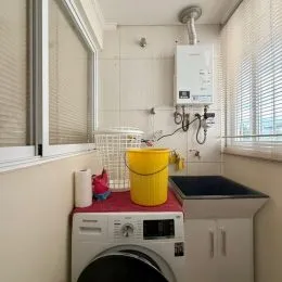 Foto de uma área de lavanderia com máquina de lavar e um recipiente amarelo.
