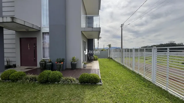 Fachada de um imóvel residencial com jardim e cerca de madeira.