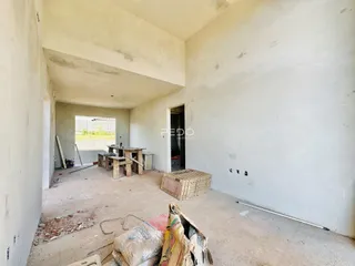 Interior de uma sala com paredes brancas e piso de concreto em obra.