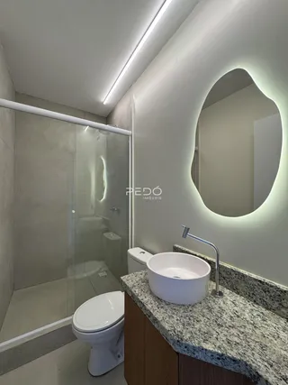Foto interna de um banheiro moderno com box de vidro e bancada de granito.