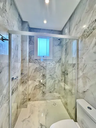 Interior de um banheiro com revestimento em mármore claro e box de vidro.
