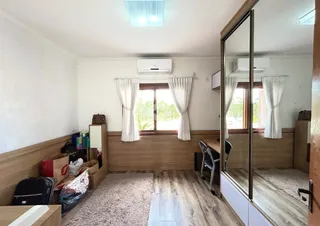 Quarto com piso de madeira e janelas com cortinas brancas.