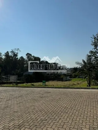 Vista externa de uma área pavimentada com árvores sob um céu azul.