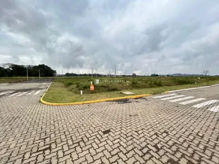 Vista externa de uma área pavimentada com grama e árvores sob um céu nublado.
