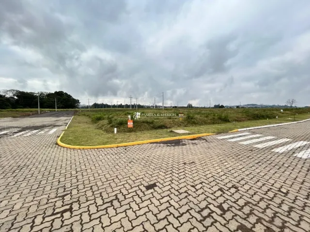 Vista externa de uma área pavimentada com grama e árvores sob um céu nublado.