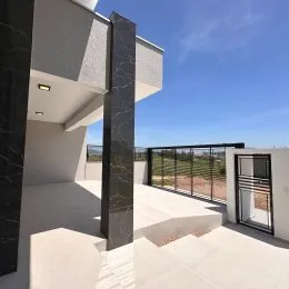 Vista externa de uma varanda com piso claro e grade escura.