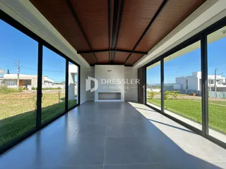 Vista interna de uma sala com grandes janelas de vidro voltadas para o exterior.