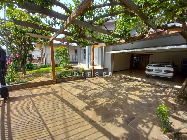 Área externa pavimentada sob uma estrutura de madeira com vegetação.