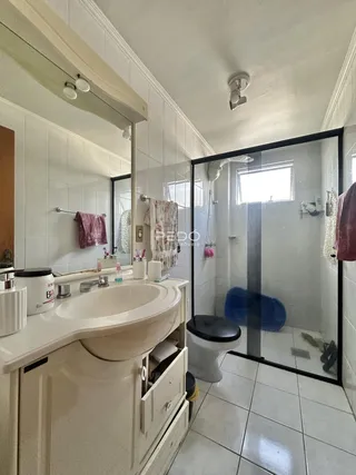 Interior de um banheiro com revestimento cerâmico e box de vidro.