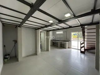 Espaço interno com teto de estrutura metálica exposta e piso de cerâmica.