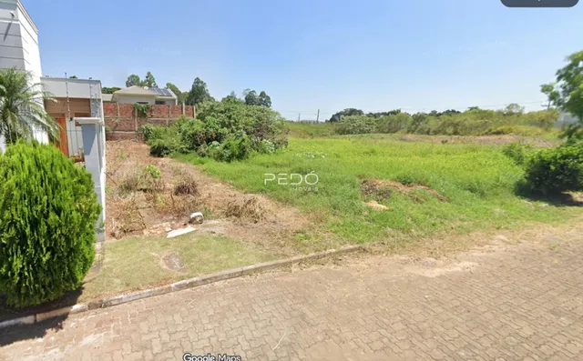 Vista externa de uma propriedade com área gramada e vegetação ao fundo.