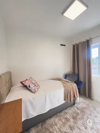 Quarto com cama e cortinas em ambiente claro.