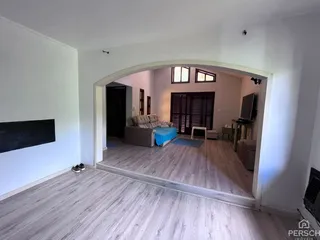 Ambiente interno com piso de madeira clara e passagem para outra área.