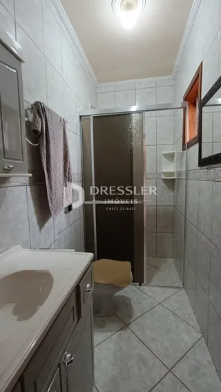 Interior de um banheiro com revestimento cerâmico e box de vidro.