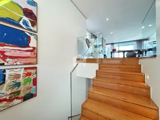 Vista interna de uma sala com parede branca e escadaria de madeira.